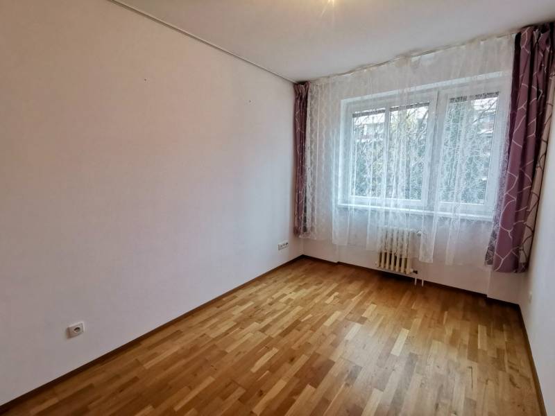 Ein Zimmer mit hellen Wänden, einem Boden mit Holzdekor, einem Fenster mit Vorhängen in einer 4-Zimmer-Wohnung.