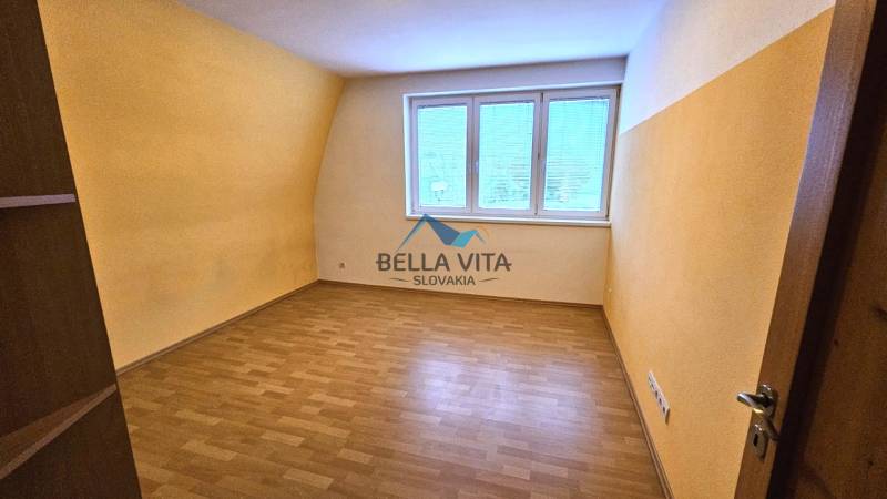 Ein Zimmer mit einem Fenster, gelben Wänden und einem Boden in Holzoptik in einem Gebäude.