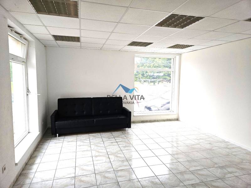 Izba s čiernou pohovkou, svetlými stenami, dlažbou a veľkými oknami v budove.