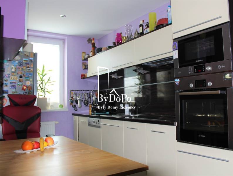 Küche in einer Einzimmerwohnung mit einem hellen Schrank, einem Stuhl und Obst auf dem Tisch.