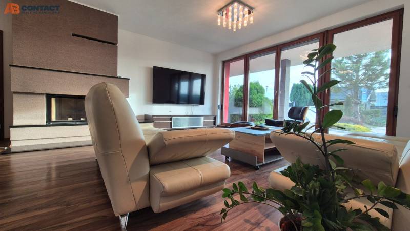 Wohnzimmer eines Einfamilienhauses mit Ledersofa, Kamin, Fernseher und Boden in Holzoptik.