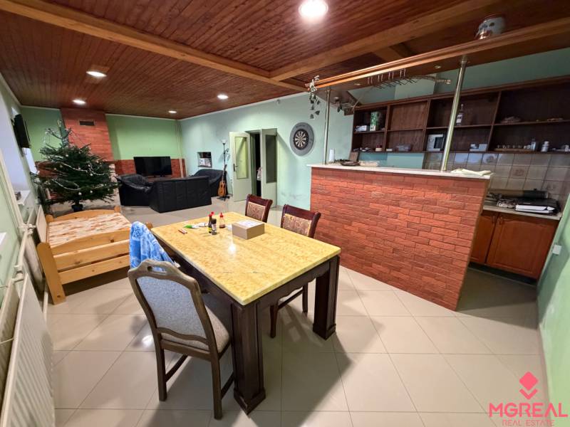 Wohnzimmer eines Einfamilienhauses mit einer Theke aus Ziegelsteinen, einem Essbereich, einem Sofa und einem Boden in Holzoptik.