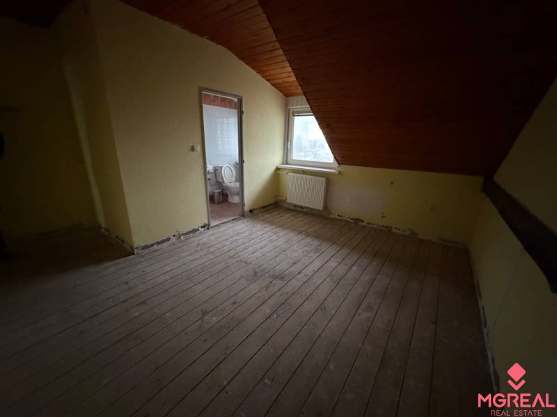 Ein Zimmer im Dachgeschoss eines Einfamilienhauses mit Holzbalkendecke und Blick auf die Stadt.