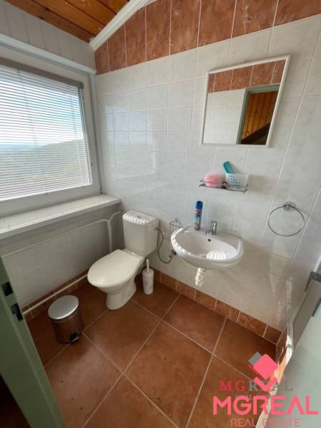 Badezimmer im Einfamilienhaus mit Toilette, Waschbecken, Fliesen und Fenster mit Jalousien.