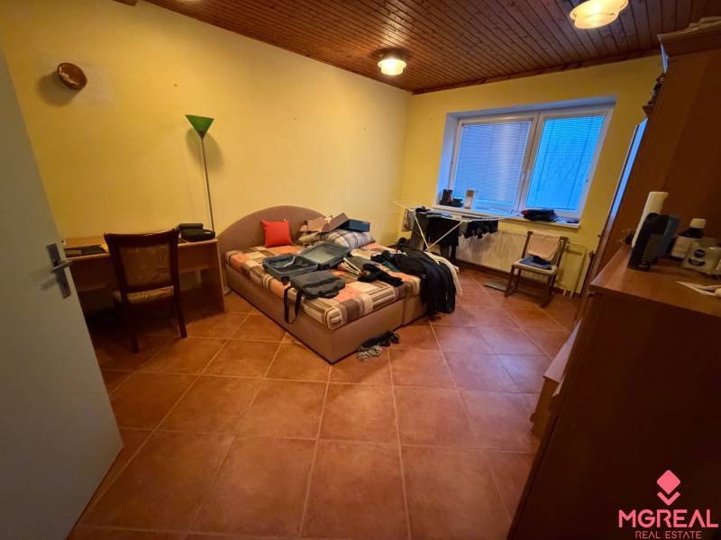 Schlafzimmer in einem Einfamilienhaus mit Bett, Tisch, Stuhl und Boden in Holzoptik.