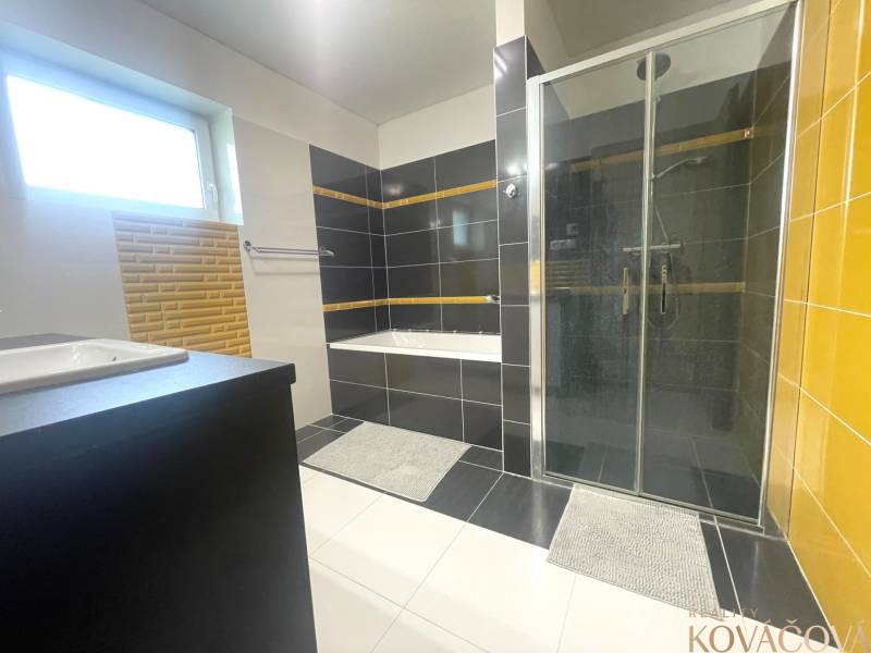 Badezimmer im Einfamilienhaus mit Badewanne, Dusche und Fenster, schwarz-weiße Fliesen.