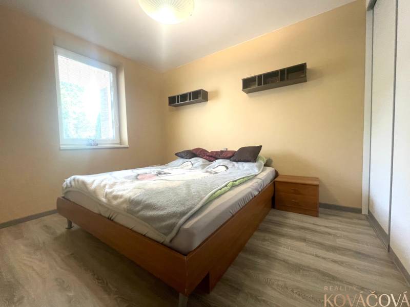 Schlafzimmer im Einfamilienhaus mit Bett, Nachttisch und Boden in Holzoptik.