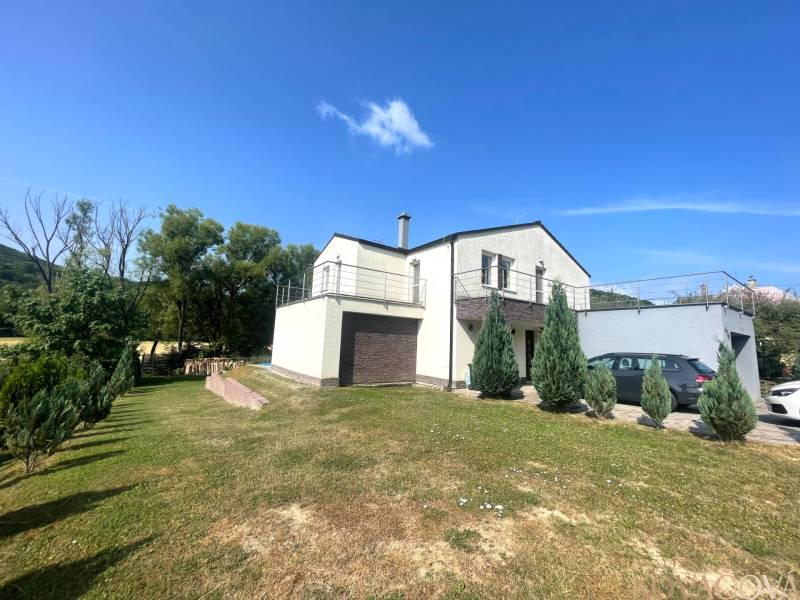 Ein Einfamilienhaus in Melčice-Lieskové mit einem weitläufigen Garten und einer Terrasse, mit einem Auto auf der Zufahrt.