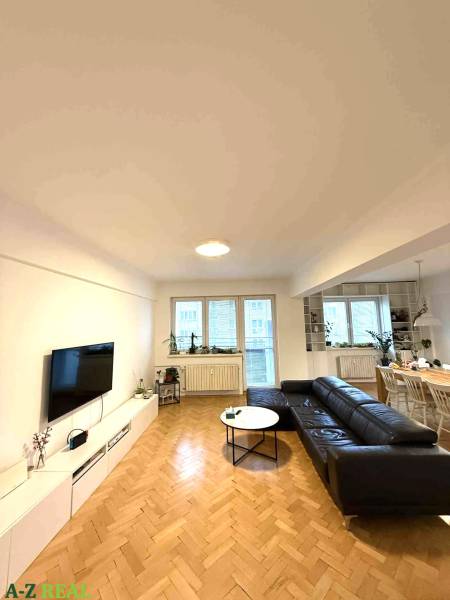 Wohnzimmer in einer 4-Zimmer-Wohnung mit Holzboden und schwarzem Sofa.