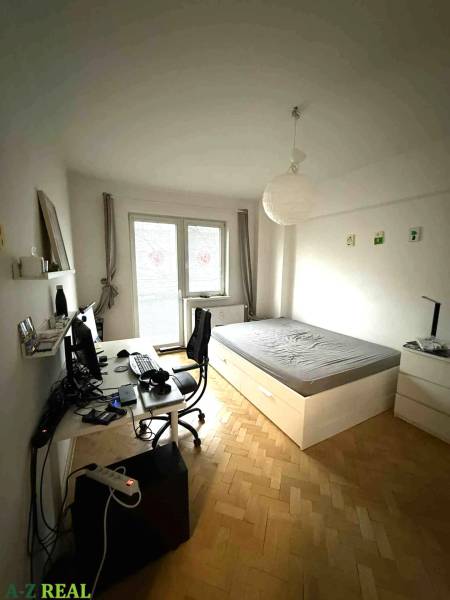 Schlafzimmer in einer 4-Zimmer-Wohnung mit Schreibtisch und Bett, Boden mit Holzdekor.