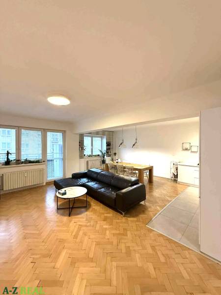 Wohnzimmer in einer 4-Zimmer-Wohnung mit Holzboden und schwarzem Sofa.