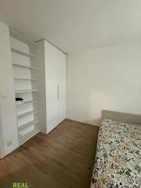 Schlafzimmer mit Schrank, Regalen und Bett in einer Vierzimmerwohnung. Boden mit Holzdekor.