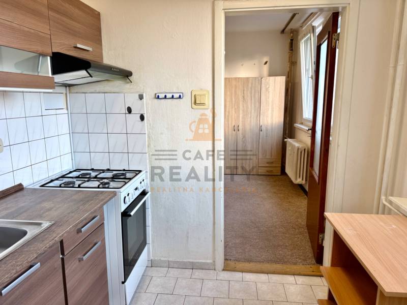 Küche mit weißen Fliesen, Herd, Schränken und Blick in den Flur in einer Einzimmerwohnung.