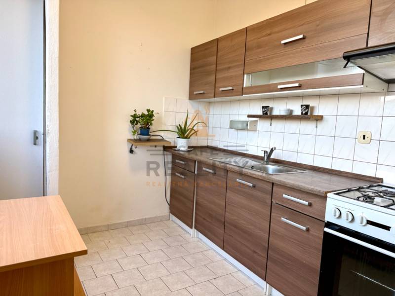 Küche mit Küchenzeile und Herd in einer Einzimmerwohnung, helle Fliesen, Holzelemente.