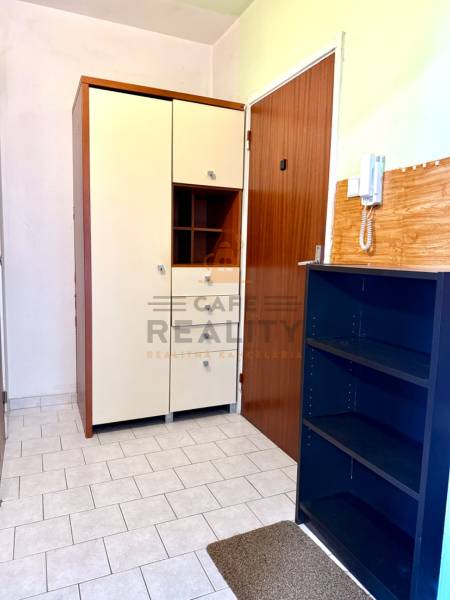 Der Flur einer Einzimmerwohnung mit Fliesen, Schränken und einem Telefon an der Wand.