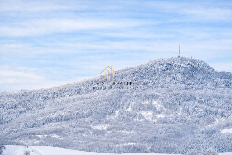 Verschneite Landschaft mit dichtem Wald und einem Sendemast auf einem Hügel bei Banská Štiavnica.