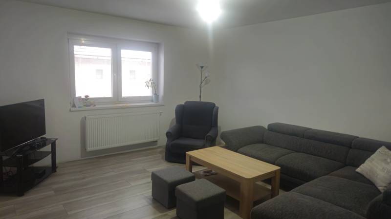 Wohnzimmer in einem Einfamilienhaus mit Sofa, Sessel und Fernseher, Boden mit Holzdekor.