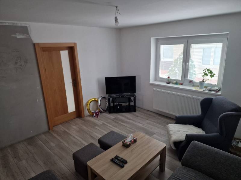 Wohnzimmer in einem Einfamilienhaus mit Holzboden, Fernseher und Sitzgelegenheiten.