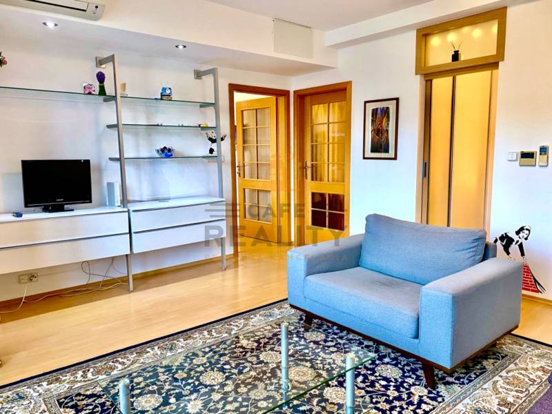 Wohnzimmer mit Sofa, Regalen, Teppich und Holzboden in einer Zweizimmerwohnung.