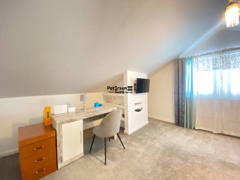 Ein Zimmer in einem Einfamilienhaus mit einem Schreibtisch, einem Fernseher und einem hellen Teppich.