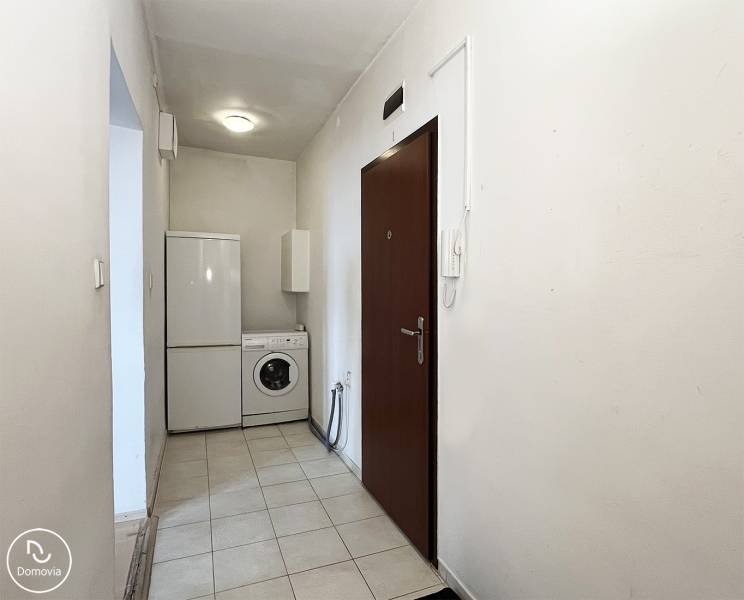 Eingangsbereich einer Einzimmerwohnung mit Waschmaschine und Kühlschrank. Weiße Wände, Keramikboden.