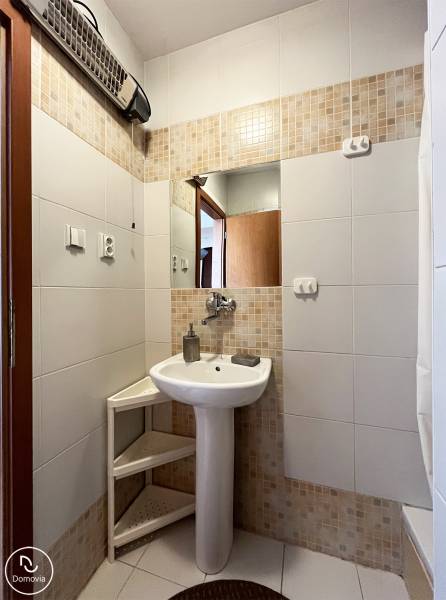 Badezimmer in einer Einzimmerwohnung mit Waschbecken, Spiegel und weißen Fliesen.