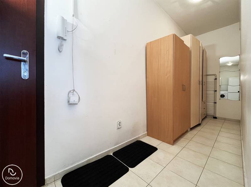 Flur in einer Einzimmerwohnung mit weißen Wänden, Fliesen und Schränken.