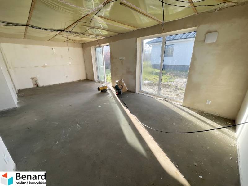 Ein leerer Raum mit großen Fenstern in einem Einfamilienhaus, ohne Bodenbelag.