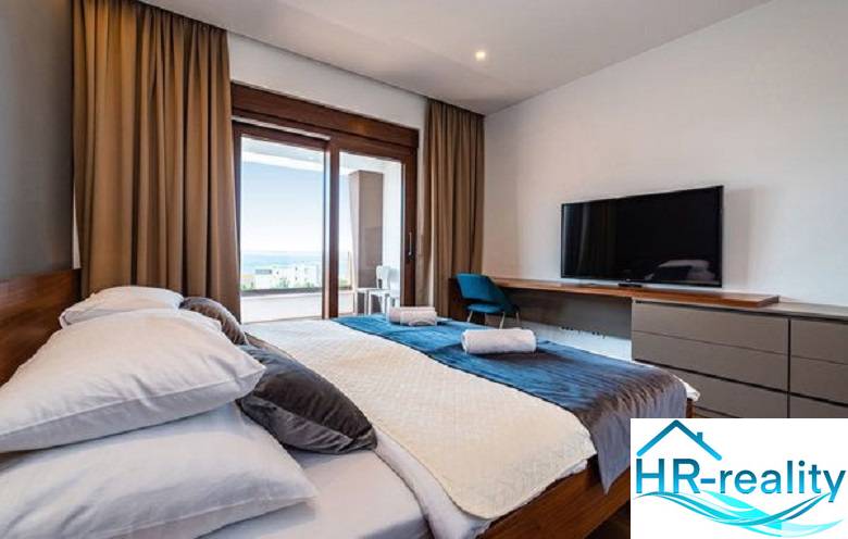 Schlafzimmer in der Villa mit Holzboden, Bett, Fernseher und Blick auf die Terrasse.