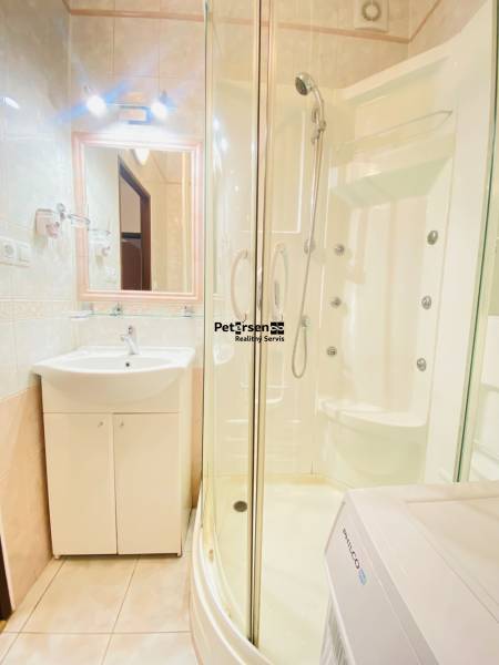 Badezimmer mit Eckdusche, Waschbecken und Waschmaschine in einer 2-Zimmer-Wohnung.