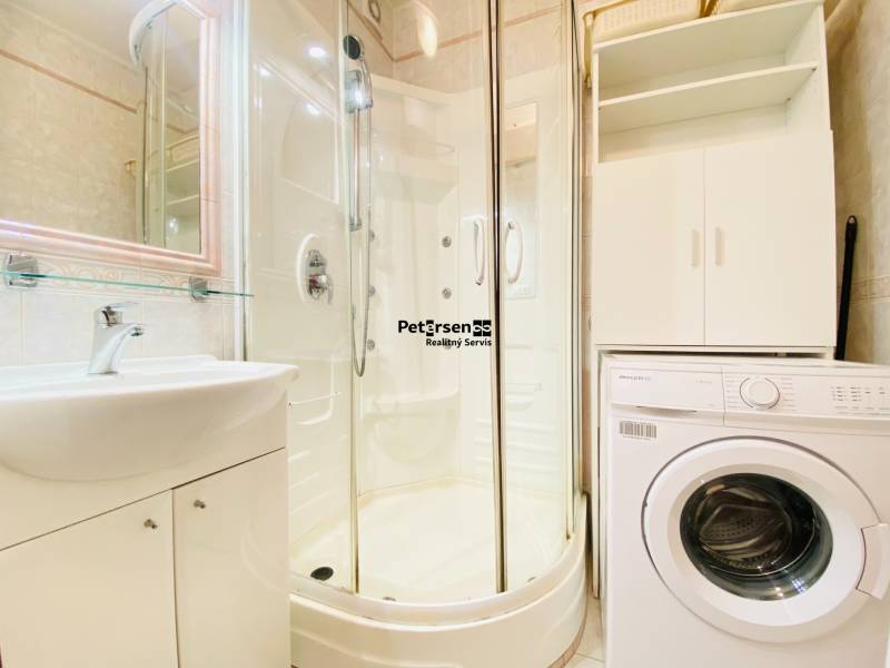 Badezimmer in einer 2-Zimmer-Wohnung mit Waschmaschine, Duschkabine und Waschbecken.