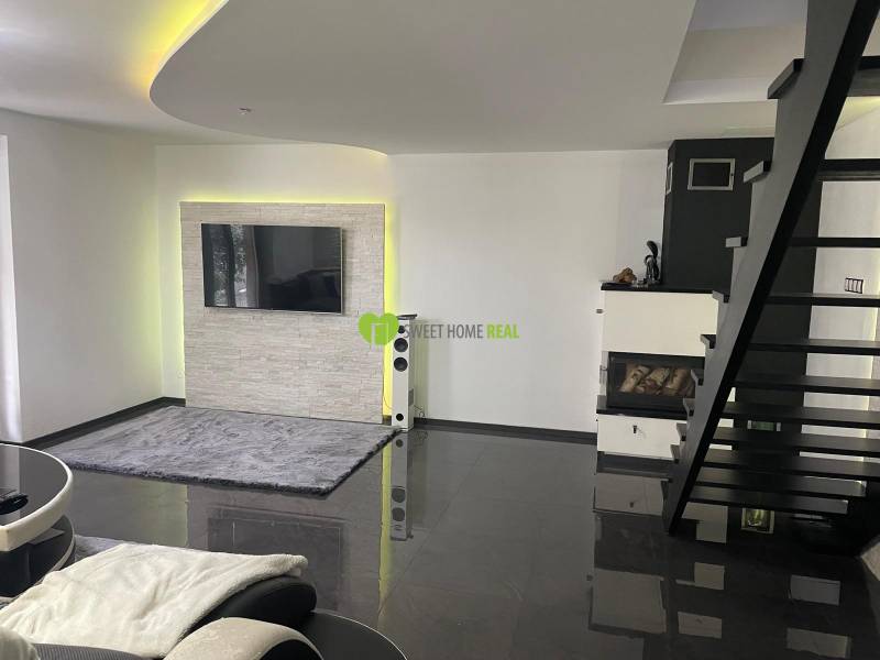 Wohnzimmer in einem Einfamilienhaus mit Treppe, Kamin und Fernseher an der Wand.