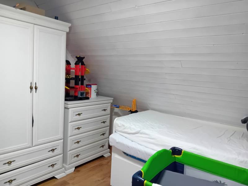 Innenraum eines Einfamilienhauses mit Bett, weißem Schrank und Boden in Holzoptik.