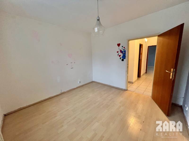 Ein Zimmer mit einem Holzboden in einer 3-Zimmer-Wohnung, helle Wand, offene Tür.