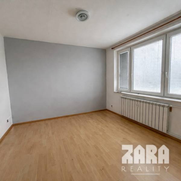 Ein leerer Raum in einer 3-Zimmer-Wohnung mit Holzboden und Fenstern mit Jalousien.