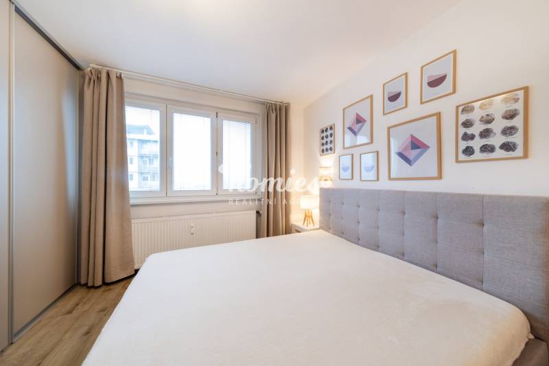 Helles Schlafzimmer mit Holzdekorboden, Bett und Wandbildern in einer Zweizimmerwohnung.