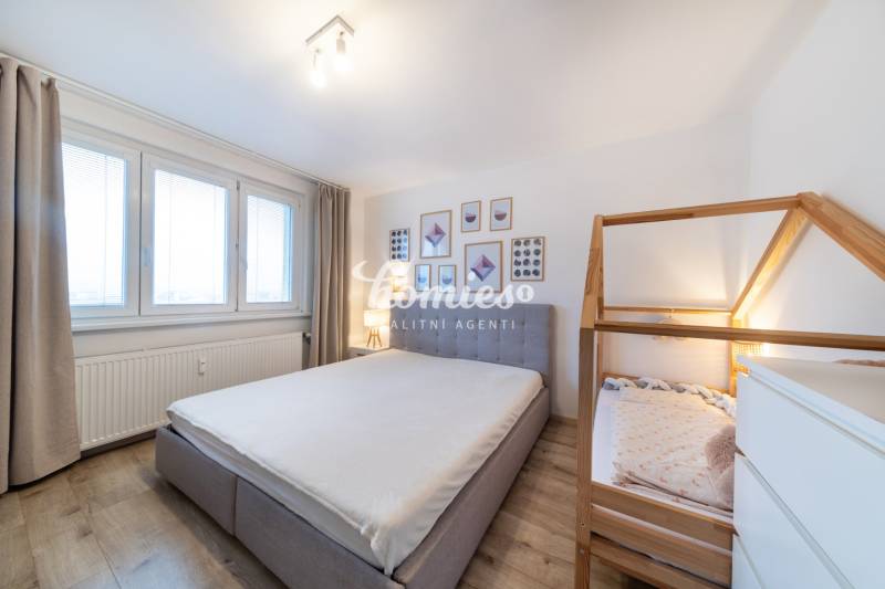 Schlafzimmer in einer 2-Zimmer-Wohnung mit Holzboden, großen Fenstern und einem Kinderbett.