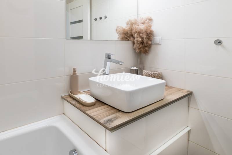 Badezimmer in einer 2-Zimmer-Wohnung mit Waschbecken, Boden in Holzoptik und dekorativem Pflanzenarrangement.