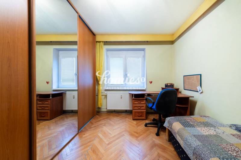 Ein Zimmer mit einem Holzboden, einem Tisch und einem Schrank in einer 3-Zimmer-Wohnung.