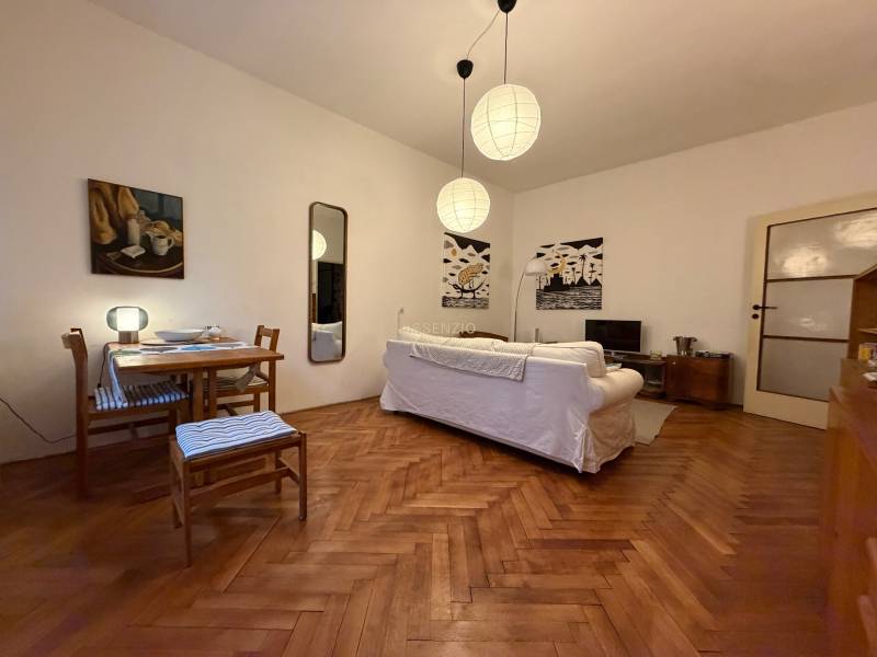 Wohnzimmer in einer Zweizimmerwohnung mit Holzboden, weißem Sofa und Tisch.