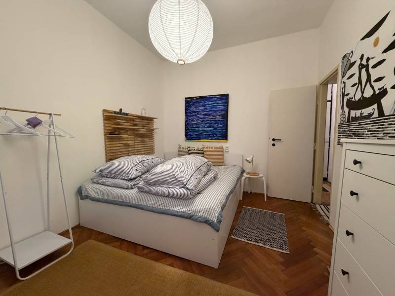 Schlafzimmer in einer 2-Zimmer-Wohnung mit Holzboden, Bett und weißem Schrank.