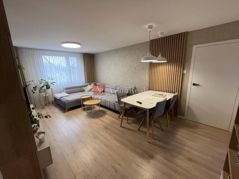 Wohnzimmer einer 4-Zimmer-Wohnung mit Holzboden, grauem Sofa und Esstisch.