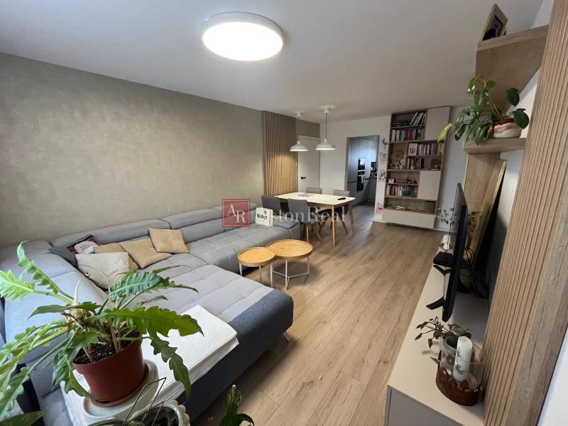 Wohnzimmer in einer Vierzimmerwohnung mit Ecksofa und Boden in Holzoptik.