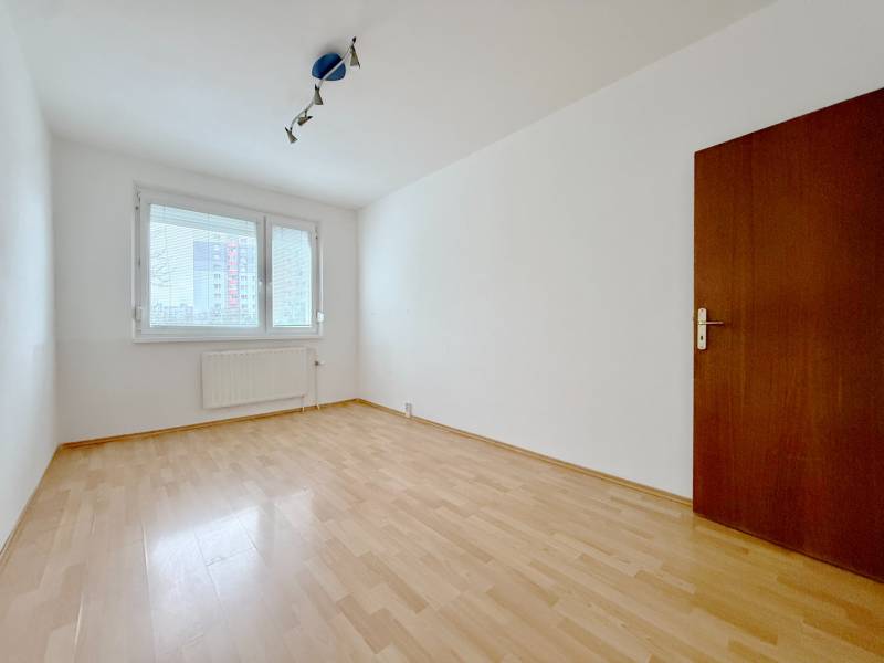 Ein leerer Raum in einer Vierzimmerwohnung mit Holzboden und einem großen Fenster.