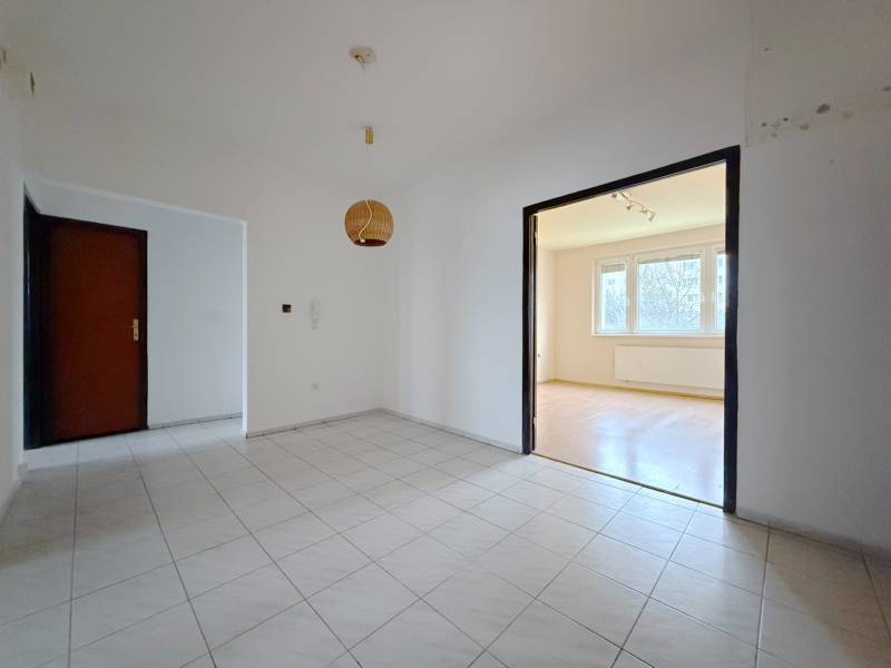 Der Flur mit Fliesen führt in ein helles Wohnzimmer mit Zugang zu einem Boden in Holzoptik.