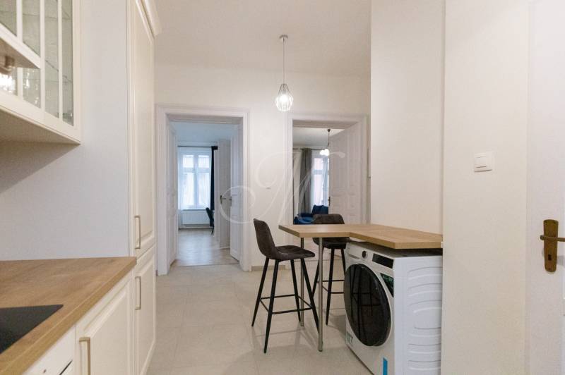 Flur in einer 3-Zimmer-Wohnung mit Waschmaschine, Stühlen und Küchenzeile.