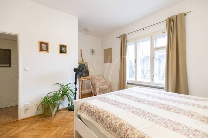 Helles Schlafzimmer mit Holzboden, Pflanzen und großen Fenstern in einer 2-Zimmer-Wohnung.