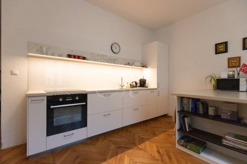 Küche in einer 2-Zimmer-Wohnung mit weißen Schränken und einem Boden in Holzoptik.