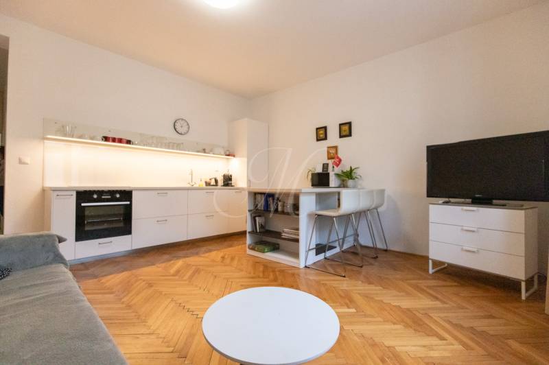 Wohnzimmer in einer 2-Zimmer-Wohnung mit Küche, Holzboden, Fernseher und Tisch.