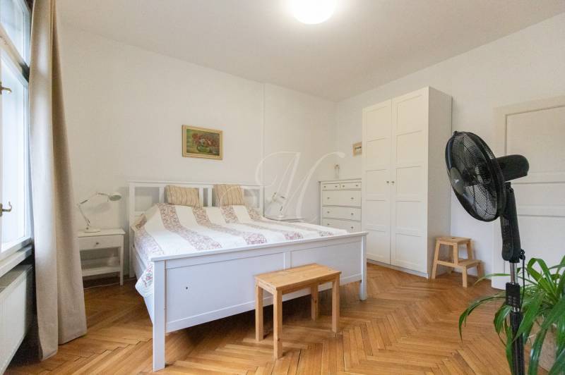 Schlafzimmer in einer Zweizimmerwohnung mit weißen Möbeln und einem Boden in Holzoptik.
